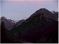 The moon stands high above the valley Cluozza at dusk
