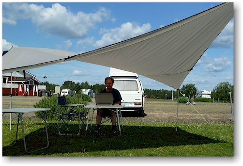 reto fuehrt im schatten unseres regendaches auf dem yllaeksen ykkoes caravan in aekaeslompolo, FI die buecher nach